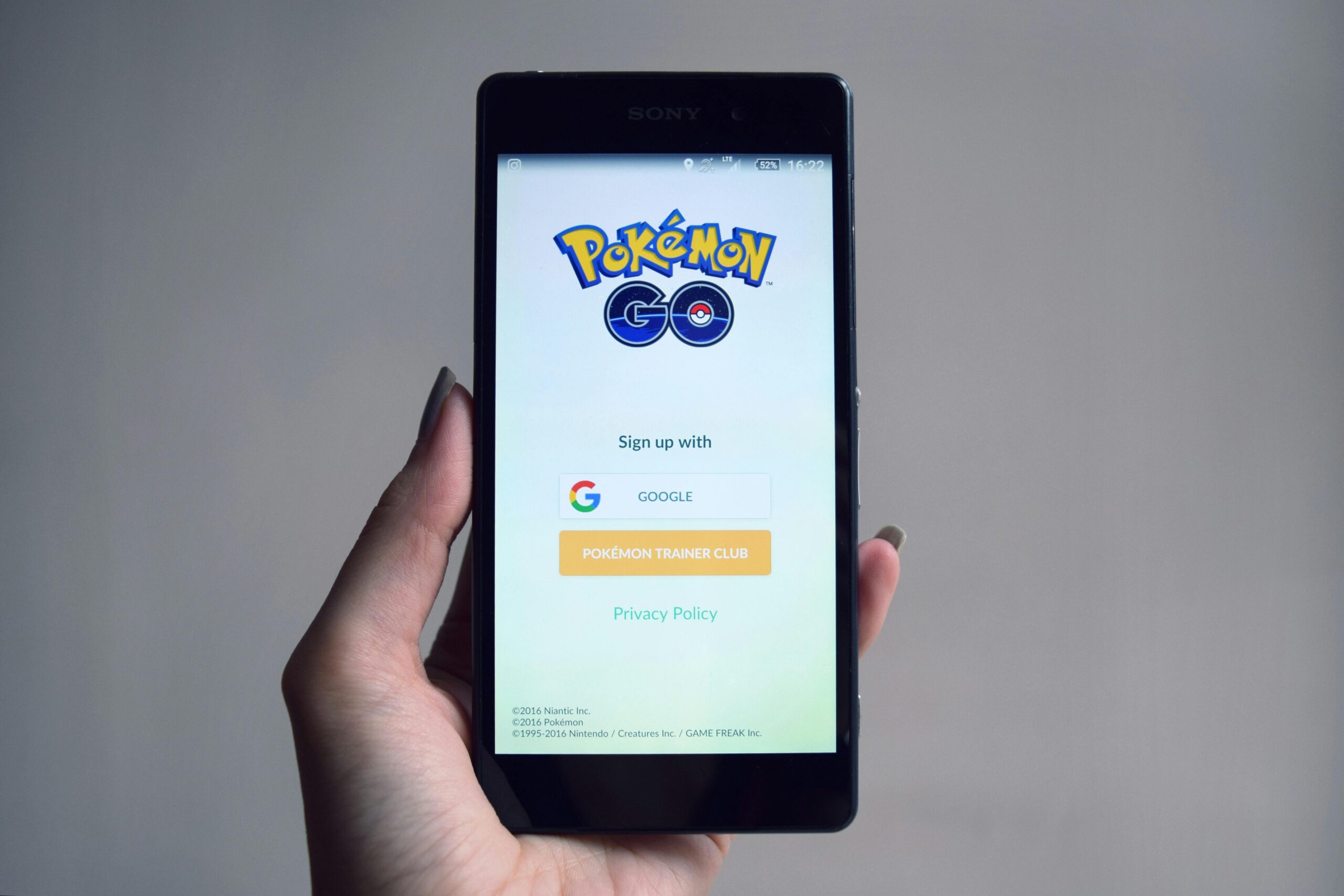 Smartphone displaying Pokémon Go app sign-in screen, held in hand.